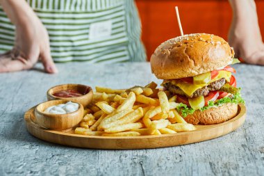 Hamburger dolu ahşap bir tabak ketçaplı patates kızartması ve mermer arka planda mayonez.