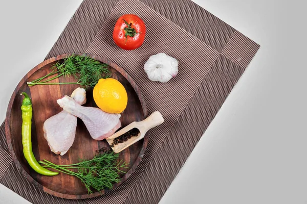 Raw chicken legs on wooden plate with greens, tomato, garlic, peppers and lemon — Stock Photo, Image