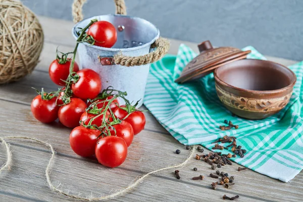 Eimer mit Tomaten und Nelken auf Holztisch mit leerer Schüssel — Stockfoto