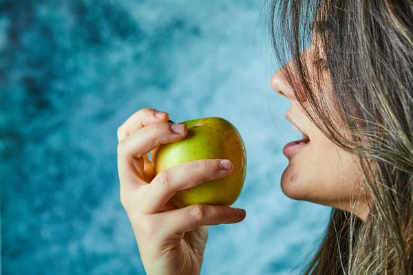 Женщина ест яблоко на голубом фоне — стоковое фото