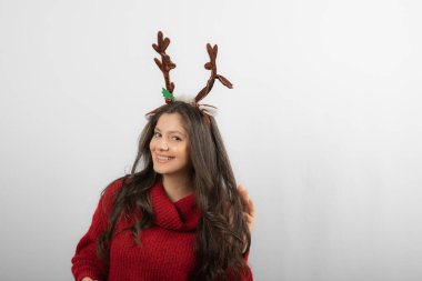 Gülümseyen bir kadın Noel boynuzu şeklinde bir saç bandıyla ayakta duruyor.