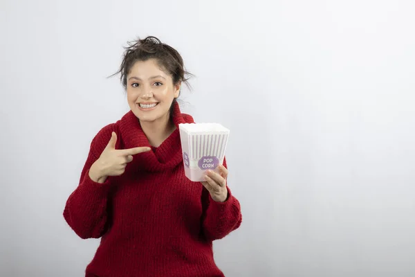 Menina em suéter apontando para um balde de pipocas — Fotografia de Stock