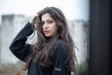 Siyah kazaklı esmer kız terasta poz veriyor.