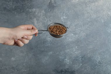 Kadın eli süzgeçle çiğ karabuğdayı süzüyor.