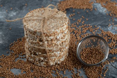 Çiğ karabuğday, süzgeç kaşığı ve mermer yüzeyde kızarmış ekmek.