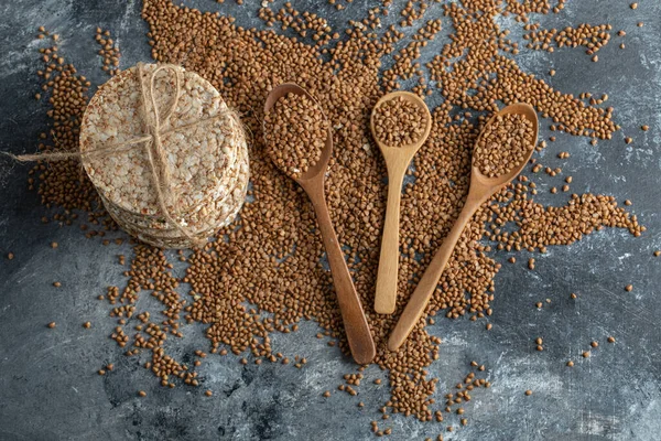 Ложки сирої гречки та смачний хрусткий хліб на мармуровій поверхні — стокове фото