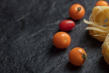 Koyu arkaplanda kiraz domatesli pişirilmemiş yuva makarnası.