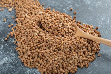 Tahta kaşık, mermer yüzeyde pişmemiş karabuğdayla dolu.