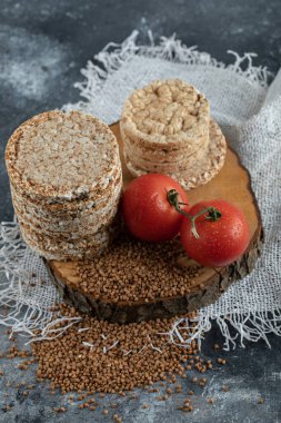 Tahta üzerinde çiğ ekmek, domates ve çiğ karabuğday yığını.