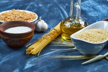 Mavi arka planda bir şişe yağlı ve sarımsaklı çeşitli pişmemiş makarna.