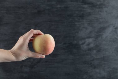 Parmaklarının arasında sarımsı bir elma tutan çiftçi.