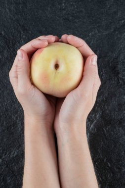 Avucunun içinde sarı şeftali tutan biri.