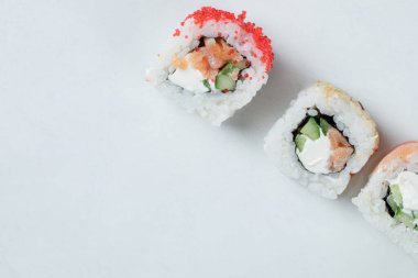 Beyaz arka planda karışık malzemelerle suşi ruloları.