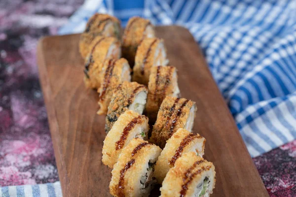 Rollos de sushi fritos con ingredientes mezclados y cubierta crujiente en un tablero de madera — Foto de Stock