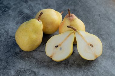 Gri mermer arka planda tam ve yarısı kesilmiş sarı armutlar.