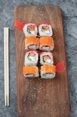 Maki, ahşap tabakta kırmızı havyar sosuyla yuvarlanıyor.