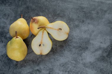 Gri mermer arka planda tam ve yarısı kesilmiş sarı armutlar.