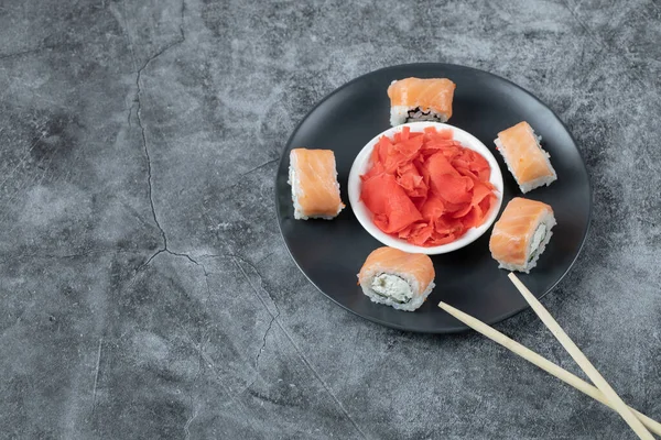 Laxsushi rullar serveras med röd ingefära på en svart tallrik — Stockfoto