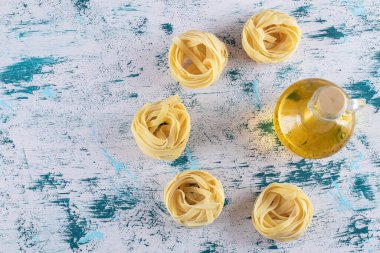 Tagliatelle yuvaları ve mavi arka planda bir bardak zeytinyağı