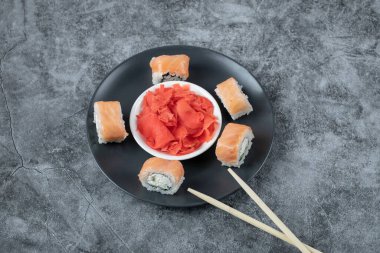 Siyah tabakta marine edilmiş kırmızı zencefilli somon ruloları.