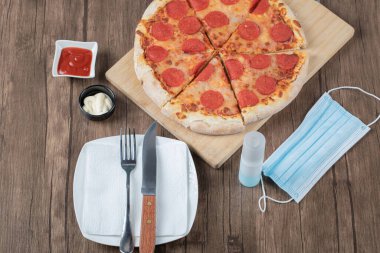 Biberli pizza ahşap bir tahtanın üzerinde sos, tabak, el dezenfektanı