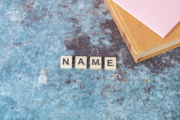Nombre escrito con letras negras en dados de madera con un libro antiguo alrededor —  Fotos de Stock
