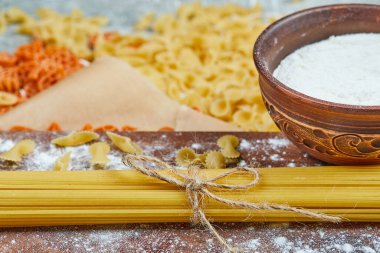 Türlü türlü pişmemiş makarna ve gri arka planda bir kase un