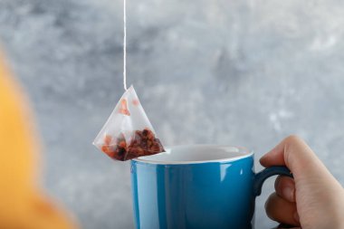 Mavi bir fincanla çay poşetini tutarken