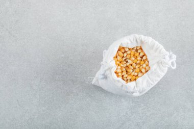 Gri arka planda mısır taneleriyle dolu beyaz bir çuval.