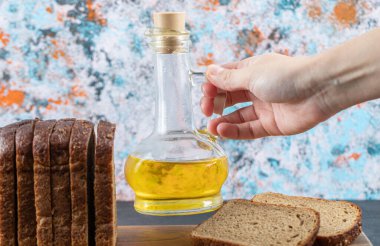 Renkli bir arka planda bir şişe yağı tutan el.