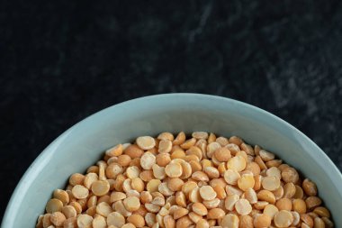 Koyu arkaplanda pişmemiş patlamış mısır olan mavi bir tabak.