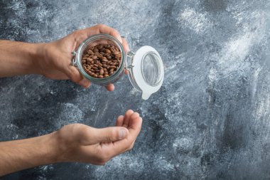 Kahve çekirdeği dolu bir kavanozu tutan erkek elleri.