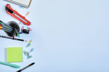 Ofis malzemeleri, defter, kalemler ve mavi arka plandaki klipler.