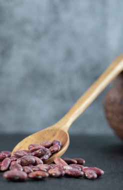 Koyu arka planda bir avuç çiğ fasulye ve tahta kaşık.