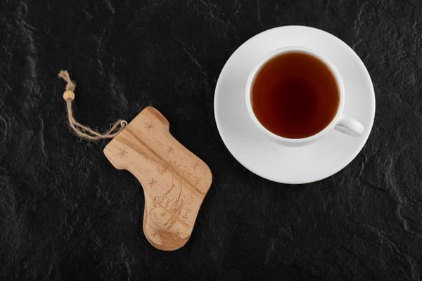 Una taza blanca de té caliente con un juguete de Navidad sobre un fondo negro — Foto de Stock