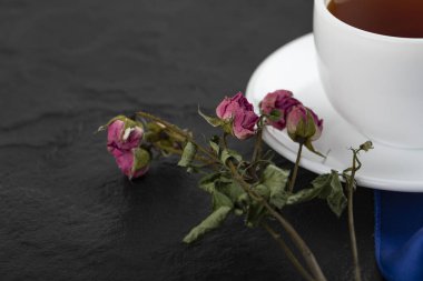 Siyah arka planda bir fincan sıcak çayla kurumuş güller.