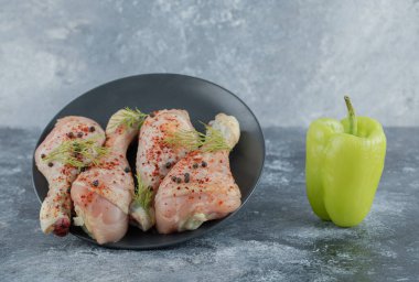 Siyah tabakta çiğ tavuk budu ve taze organik biber.