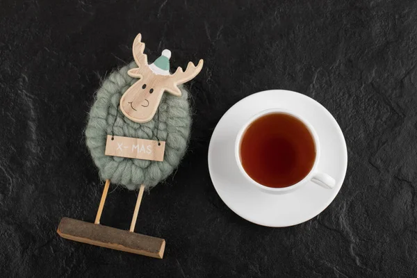 Ένα φλιτζάνι ζεστό τσάι με ένα χριστουγεννιάτικο παιχνίδι ελάφι σε μαύρο φόντο — Φωτογραφία Αρχείου