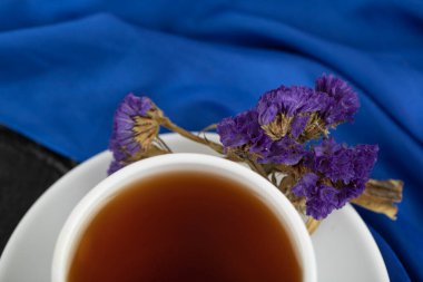 Kurumuş mor çiçekler ve siyah arka planda bir fincan sıcak çay.
