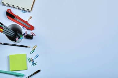 Ofis malzemeleri, defter, kalemler ve mavi arka plandaki klipler.