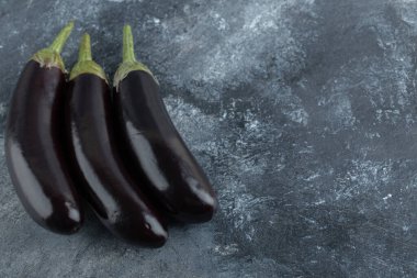 Gri arka planda üç taze patlıcan.