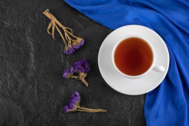 Kurumuş mor çiçekler ve siyah arka planda bir fincan sıcak çay.