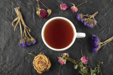 Siyah arka planda kurumuş çiçekli bir fincan çay.