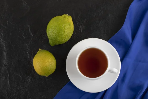 Una taza de té caliente con dos limones verdes — Foto de Stock