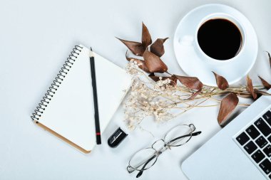 Not defteri, dizüstü bilgisayar, fare ve beyaz masada bir fincan çay.