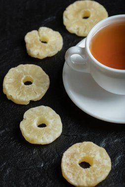 Koyu arkaplanda kurutulmuş ananas aromalı bir fincan çay.