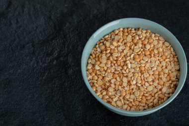 Koyu arkaplanda pişmemiş patlamış mısır olan mavi bir tabak.