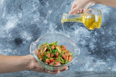 El sebze salatasına yağ döküyor.