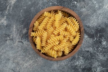 Çiğ fusilli makarna dolu ahşap bir kase.