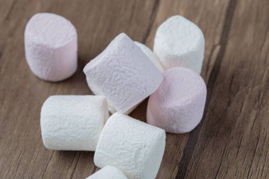 Ahşap bir tahtanın üzerinde pembe ve beyaz kabarık şekerlemeler.